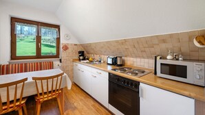 Een keuken met een eettafel, stoelen, een fornuis, een magnetron en een raam met uitzicht op een groen landschap.