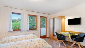 Een slaapkamer met twee bedden, een eettafel met stoelen, een televisie en grote ramen met gordijnen.