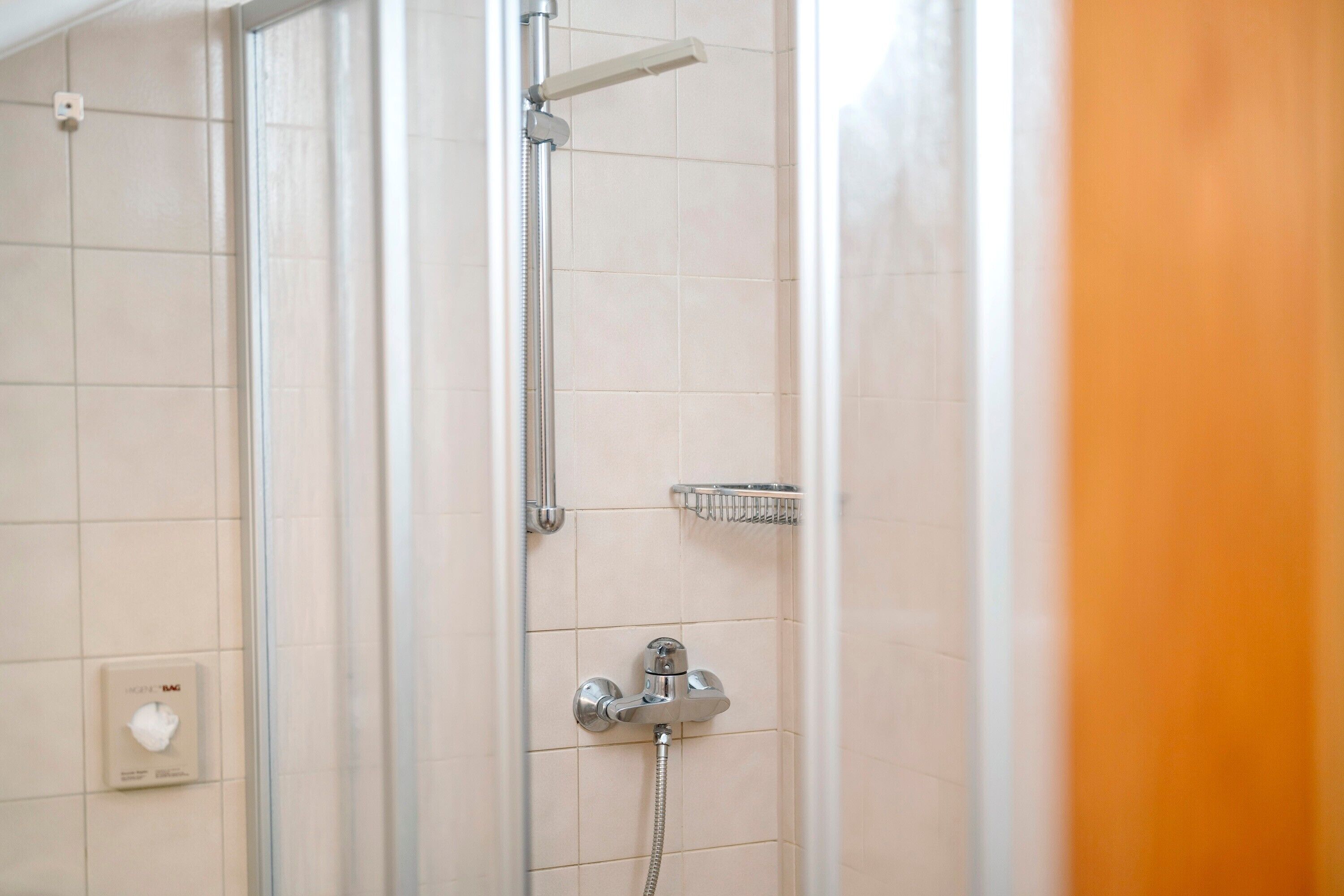 A shower with a handheld showerhead, a wall-mounted control panel, and a small shelf.