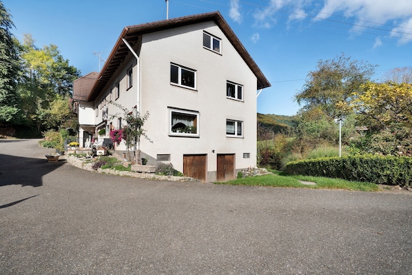 Une maison à deux étages, avec un toit en pente, un porche à l’avant et une allée.