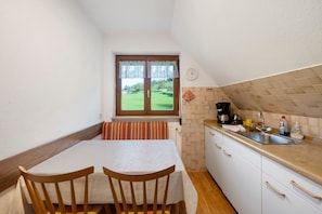 Une petite cuisine avec une fenêtre, une table à manger avec des chaises, un évier et une horloge au mur.