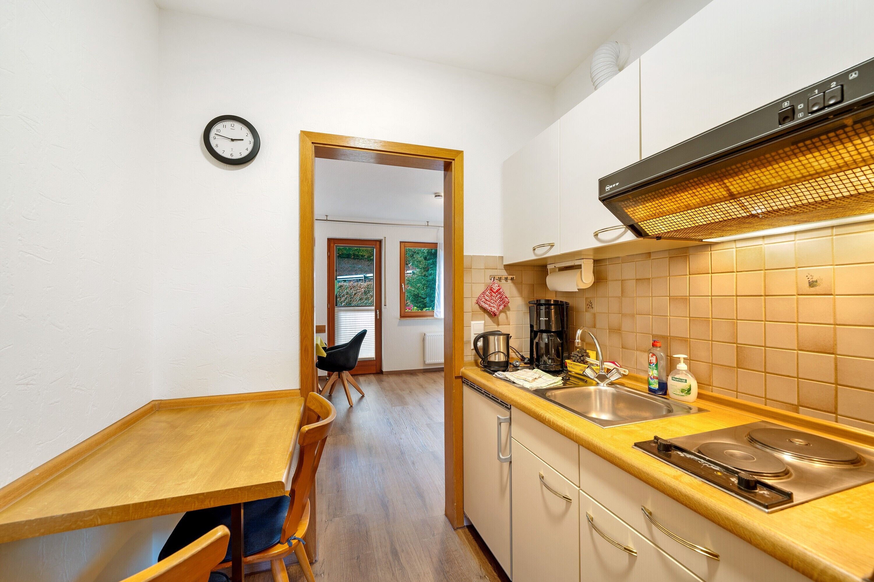 A compact kitchen with a wooden table, chairs, a sink, and a stove.