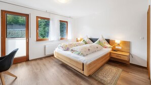 A bedroom with a wooden bed, two windows, a chair, a nightstand, and a radiator. - Apartment 'No. 2.1 Rotkelchen' with Shared Terrace, Shared Garden and Wi-Fi (Freiamt)