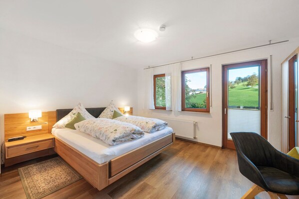 A bedroom with a bed, bedside table, lamp, and a view of a green landscape through the window.