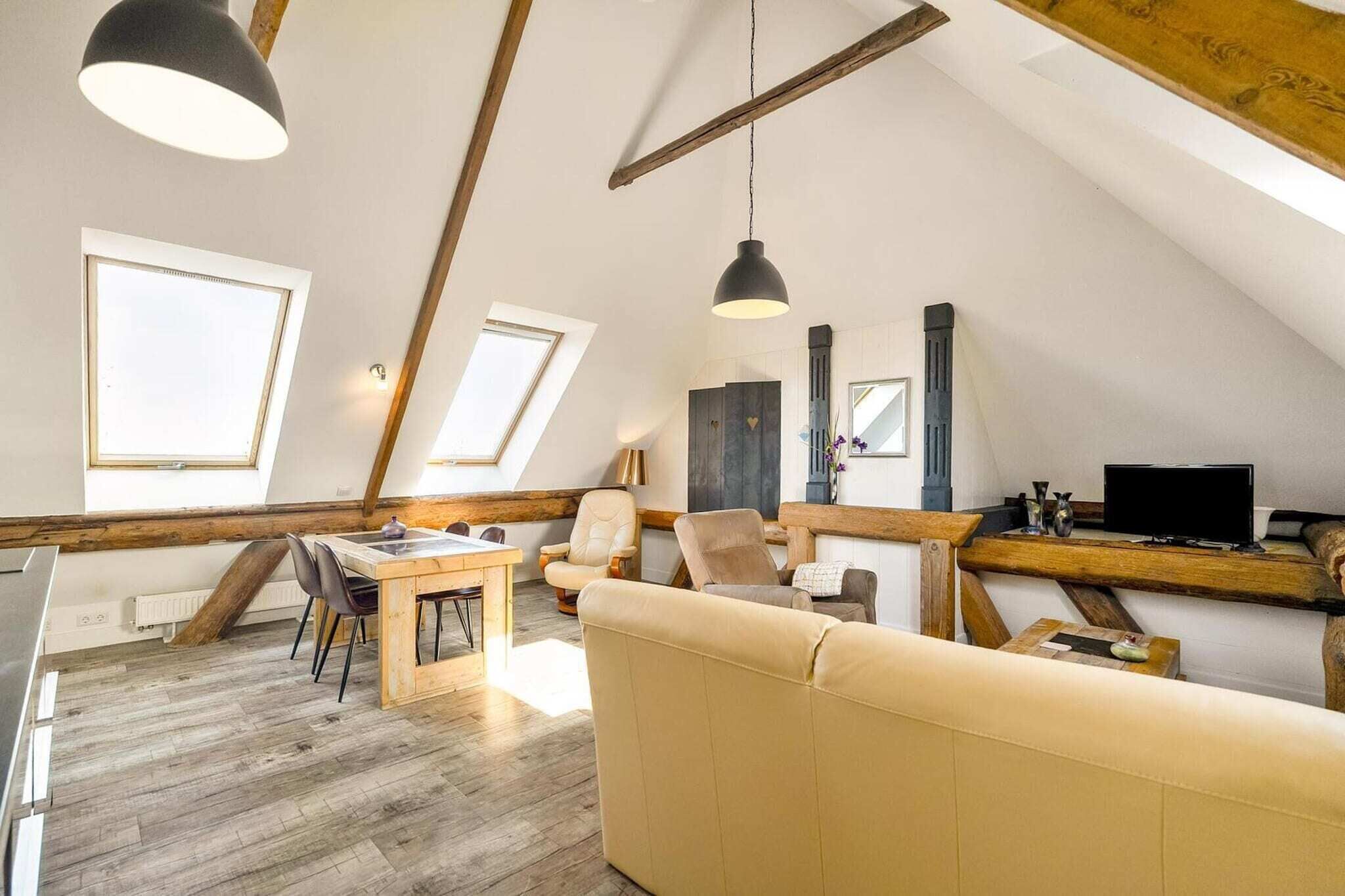 Een loft-achtige kamer met zichtbare houten balken, een bank, een eettafel en een televisie.