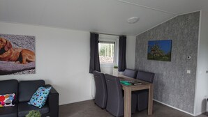 Une pièce moderne avec un canapé noir, une petite table accompagnée de deux chaises, une fenêtre avec des rideaux et deux tableaux accrochés au mur.
