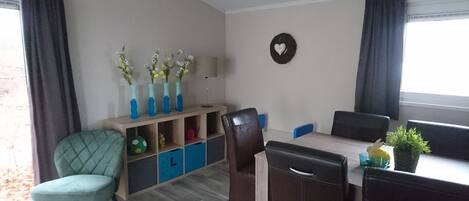 A dining area with a table, chairs, a bookshelf, and a wall-mounted decoration.
