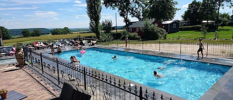A rectangular swimming pool with a black wrought iron fence, surrounded by a deck with chairs and tables.