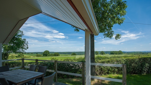 Un espace extérieur abrité, doté d’une table et de chaises, qui offre une vue sur un paysage verdoyant.