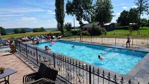 Une piscine rectangulaire entourée d’une clôture en fer forgé noir, et bordée d’une terrasse avec des chaises et des tables.