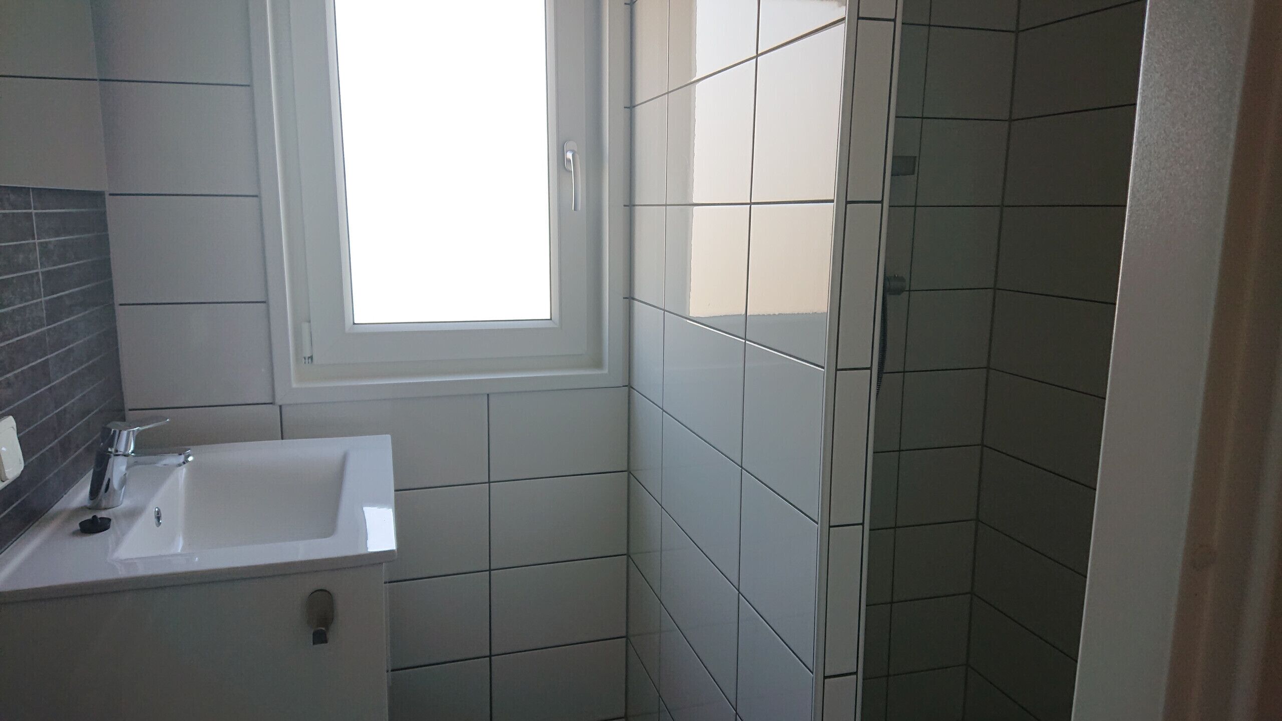 A bathroom with a white sink, a window, and tiled walls.