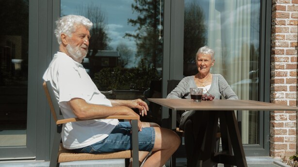Two people seated at a table with a glass window behind them.