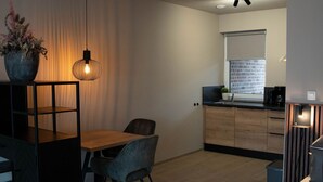 Un dormitori modern i minimalista amb un llit gran, una taula de dinar de fusta i una zona de cuina al fons.