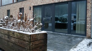 Una caixa de jardí de fusta amb plantes cobertes de neu davant d'un edifici de maó amb grans portes de vidre.