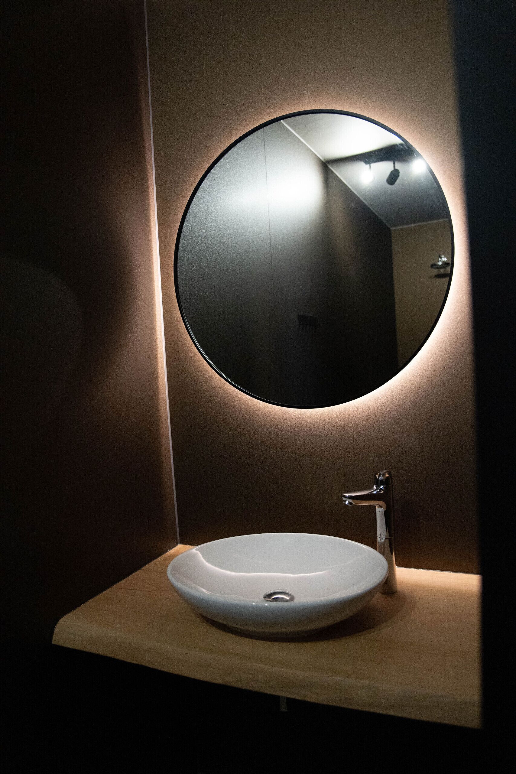 Ein modernes Badezimmer mit einem runden Spiegel, einem weißen Waschbecken und einer Holzablage.