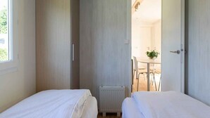 Ein Schlafzimmer mit zwei Betten, einem Heizkörper und Blick auf einen Essbereich mit Tisch und Stühlen.
