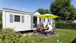 Ein Wohnmobil mit einer Terrasse, auf der eine Gruppe von Personen an einem Tisch unter einem gelben Sonnenschirm sitzt.