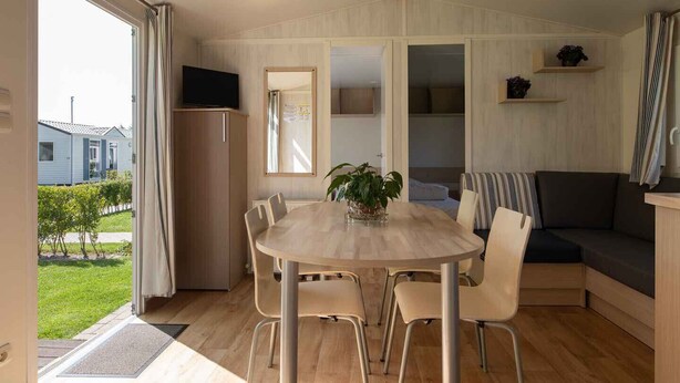 Ein gemütliches Zimmer mit einem runden Holztisch, vier Stühlen, einem dunklen Sofa und einer kleinen Pflanze auf dem Tisch.