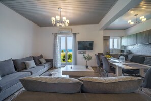 A modern living room with a sofa, a dining table, and a kitchen area. - 7 Bedroom | Alkioni Seafront Villas | 2 Villas by the Sea | Dramia | Chania, Villa (Chania)