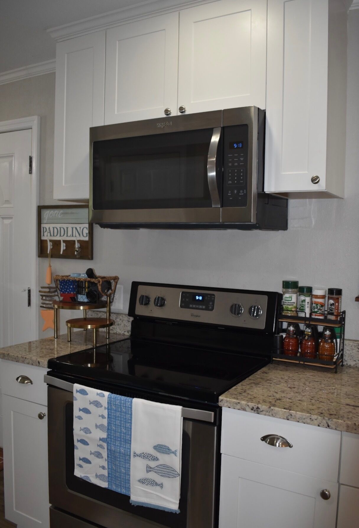 A kitchen with white cabinets, a stainless steel microwave, a black stove, and a spice rack.