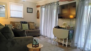 A living room with a sofa, a small wooden table, a TV, and a desk with a chair.