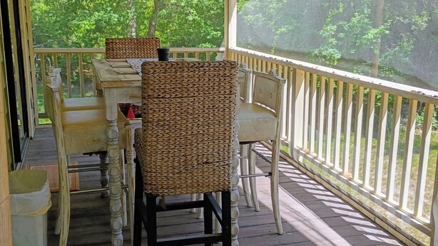 A covered outdoor seating area with wicker chairs and a table, surrounded by a wooden deck and railing.
