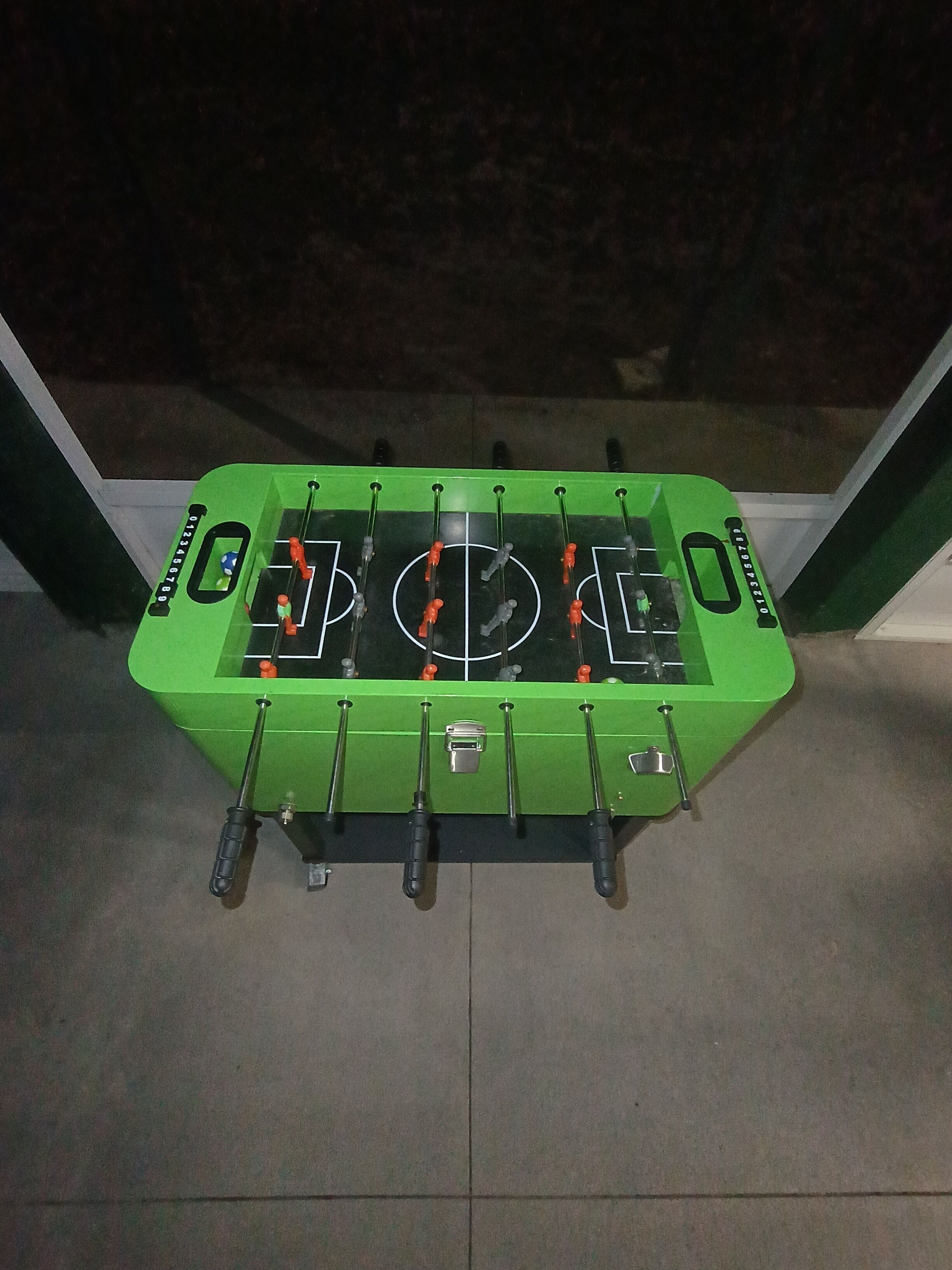 A green foosball table with a soccer field design, mounted on a wall.