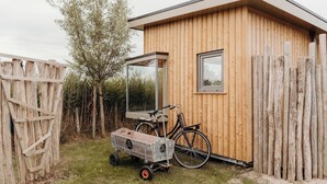 A wooden cabin with a large window, a bicycle, and a wagon. - Solglimt 2 pers holiday home with stunning views (Callantsoog)
