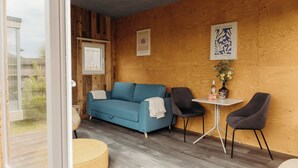 A modern room with a blue sofa, two chairs, a small table, and a window. - Solglimt 2 pers holiday home with stunning views (Callantsoog)