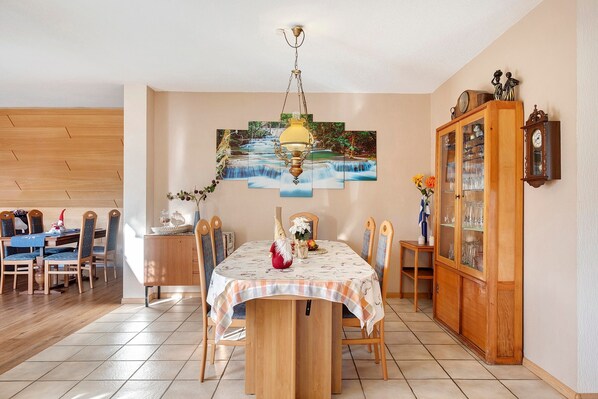A dining area with a table set for four, a wooden cabinet with glass doors, and a wall-mounted clock.