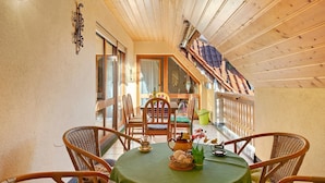 Un comedor con sillas de mimbre, una mesa con mantel verde y vista a un balcón con barandas de madera.