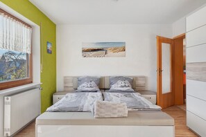 A bedroom with a bed, a window with curtains, a picture on the wall, and a door.