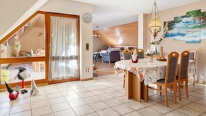 Un comedor con una mesa dispuesta para cuatro personas, una araña y una vista de una sala de estar al fondo.