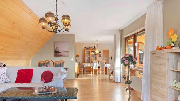 Una sala de estar con techo de madera, un comedor con mesa y sillas, y un pasillo con planta en maceta.