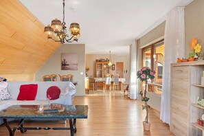 A living room with a wooden ceiling, a dining area with a table and chairs, and a hallway with a potted plant.