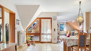 Un comedor amplio con techo alto, una mesa de madera y sillas. Hay un ventanal grande que proporciona luz natural y vistas al exterior.