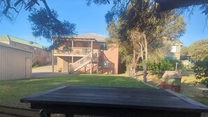 Um quintal com um deck de madeira, um prédio de tijolos com varanda e um pequeno galpão.