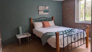 Um quarto com uma cama, uma mesinha de cabeceira, um ventilador de teto e uma janela com vista para árvores.