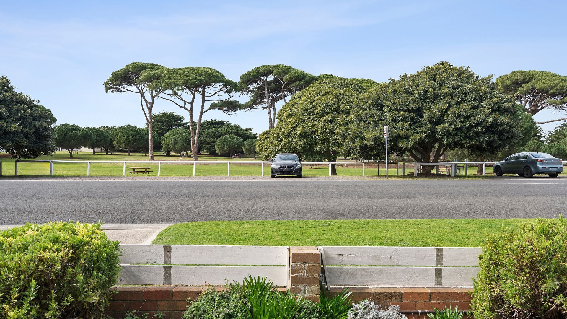 A road with two cars, a grassy area, and trees.