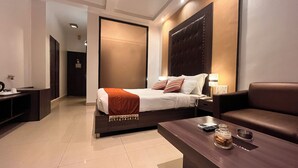 A modern hotel room with a large bed, a sofa, a coffee table, and a desk with a phone and a lamp. - The New Marrion (Bhubaneshwar)