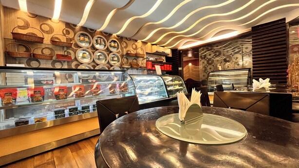 A bakery counter with a display case of pastries and a round table with a napkin holder. - The New Marrion (Bhubaneshwar)