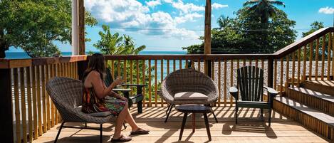 A wooden deck with a woman sitting on a wicker chair, another chair, and a small table.