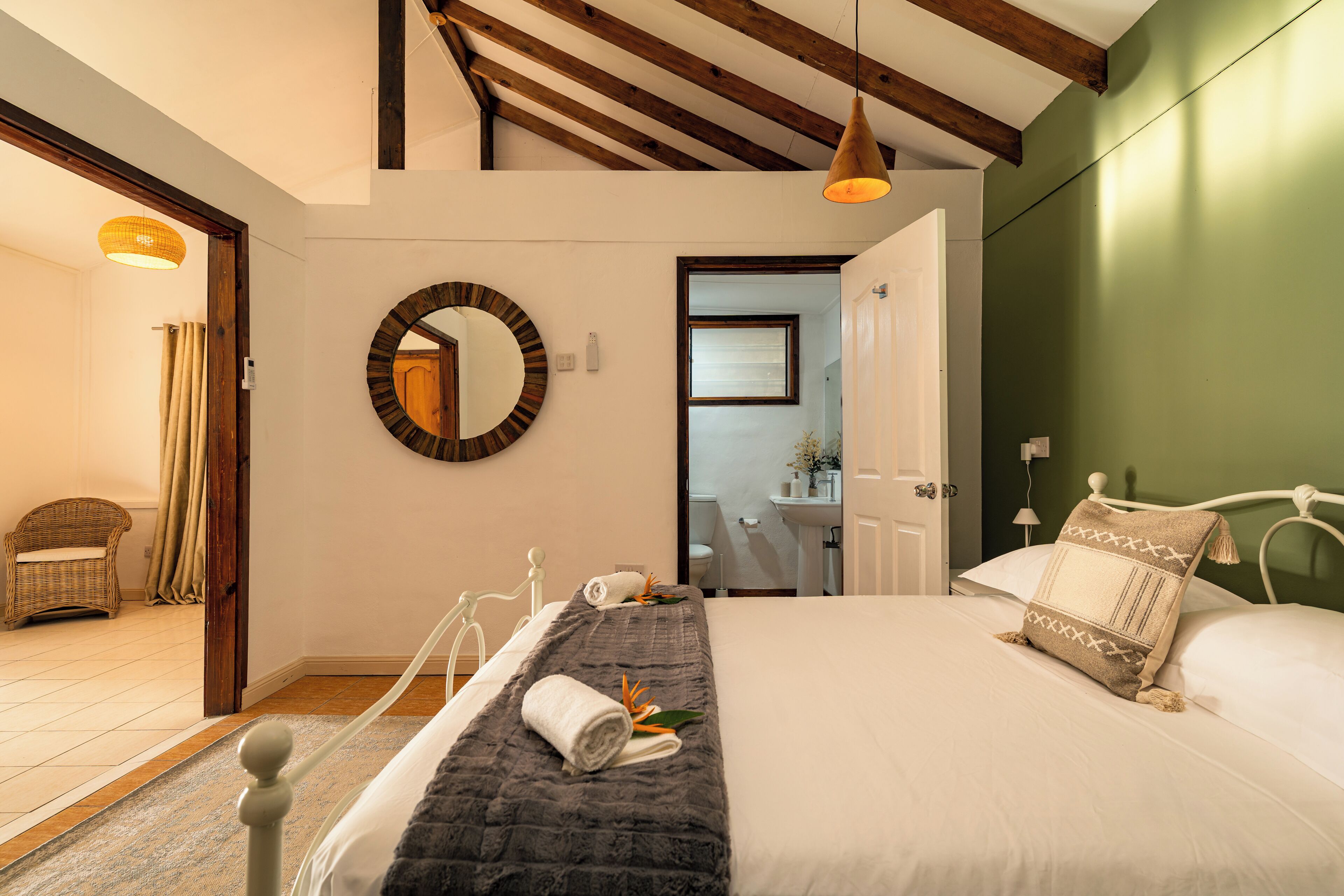 Un dormitorio con cama, espejo redondo, lámpara colgante y vista al baño.