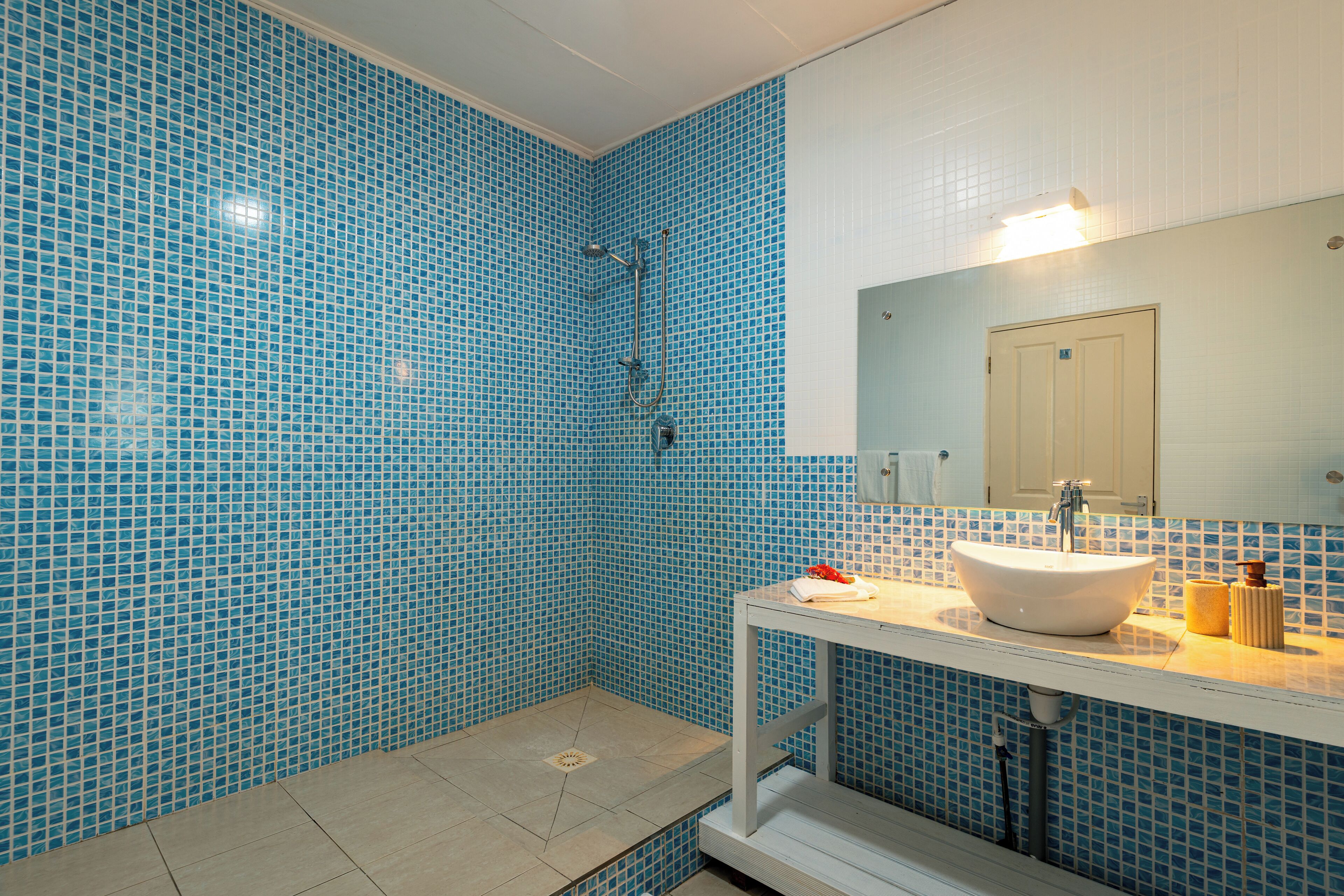 Ein Badezimmer mit blauen Mosaikfliesen, einem weißen Waschbecken und einem Spiegel darüber.