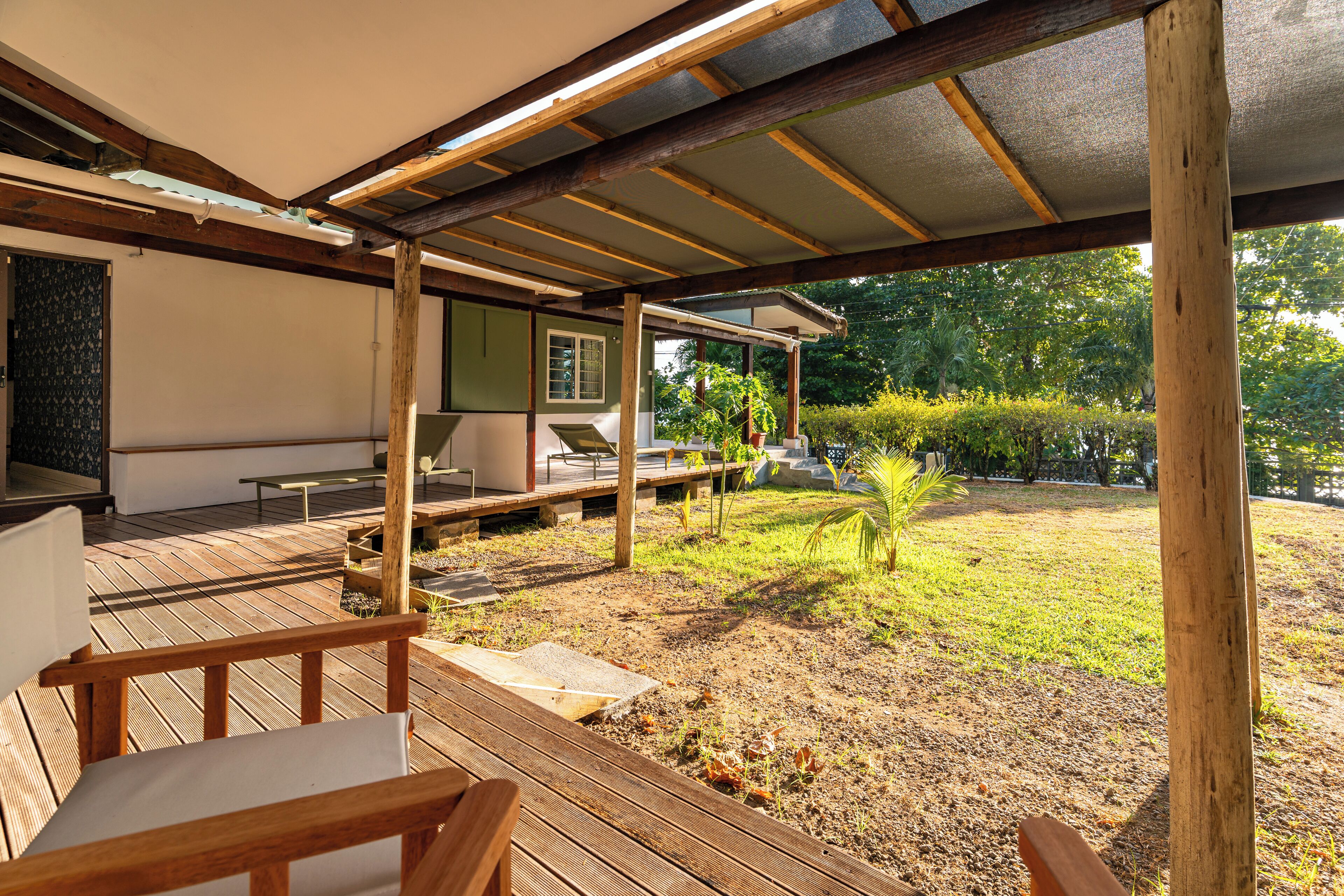 A wooden deck with outdoor furniture, a covered area with a pergola, and a view of a garden and trees.