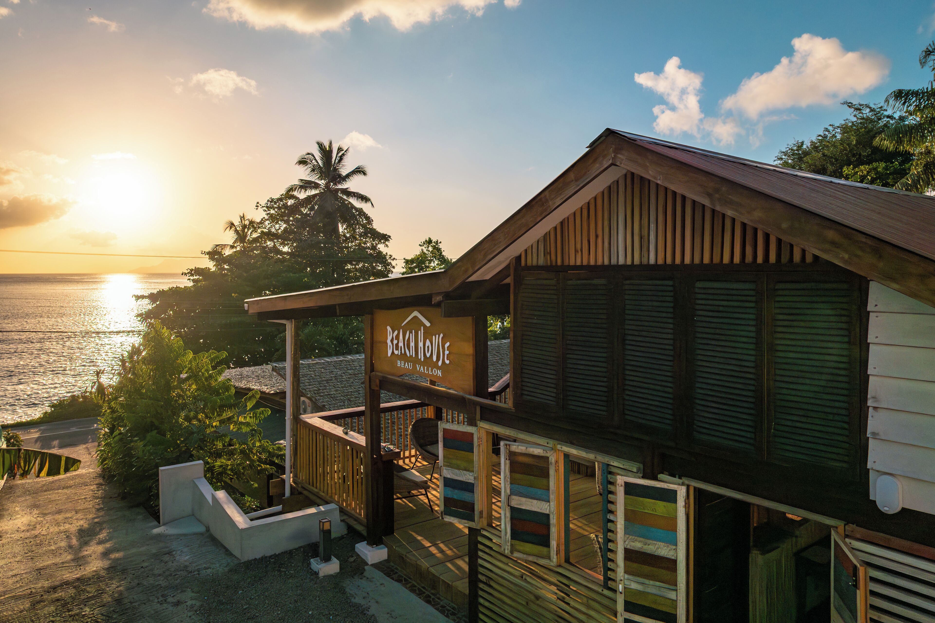 Una casa de playa con fachada de madera, un balcón y un letrero que dice 'Beach House Beau Vallon'.