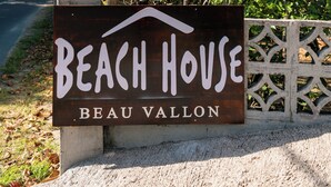 A sign for "Beach House Beau Vallon" with a view of a lush green plant and a clear blue sky in the background. - Beach House Beau Vallon (Mahe Island)