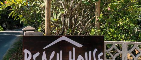 Schild für "Beach House Beau Vallon" mit Blick auf üppiges Grün und einen klaren, blauen Himmel.