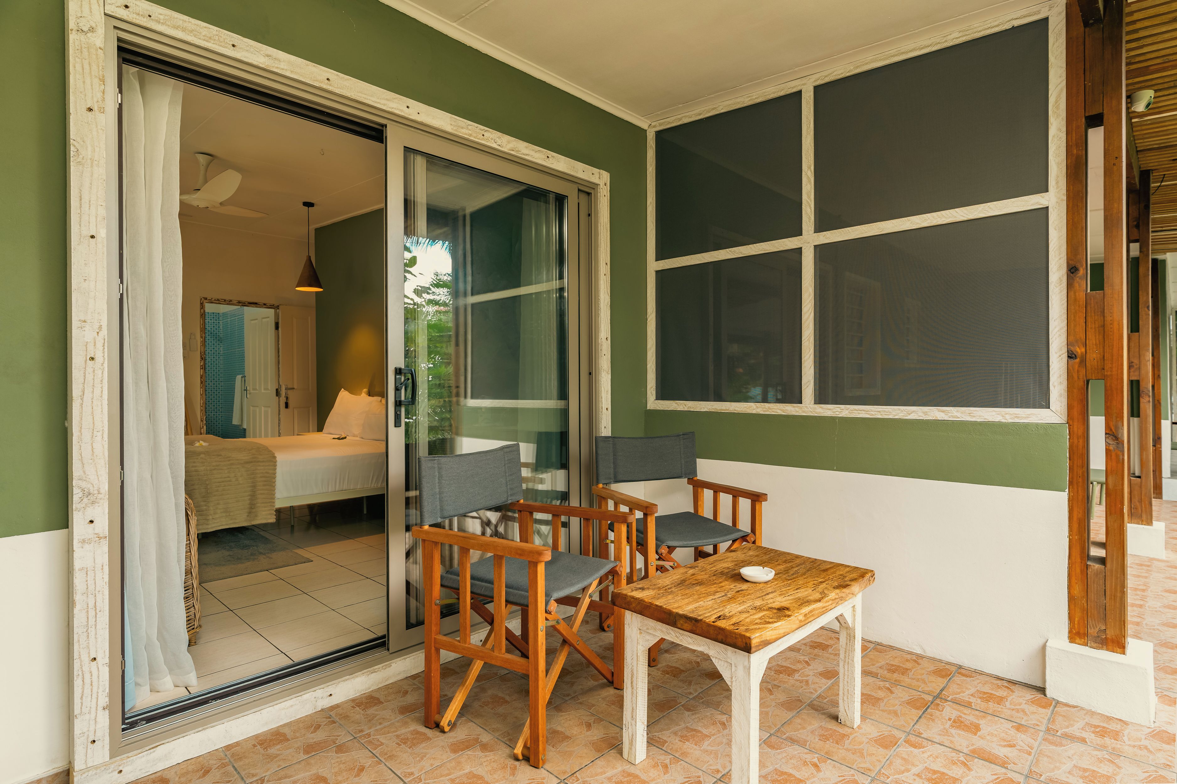 A room with a sliding glass door leading to a bathroom, a wooden table with chairs, and a large window.
