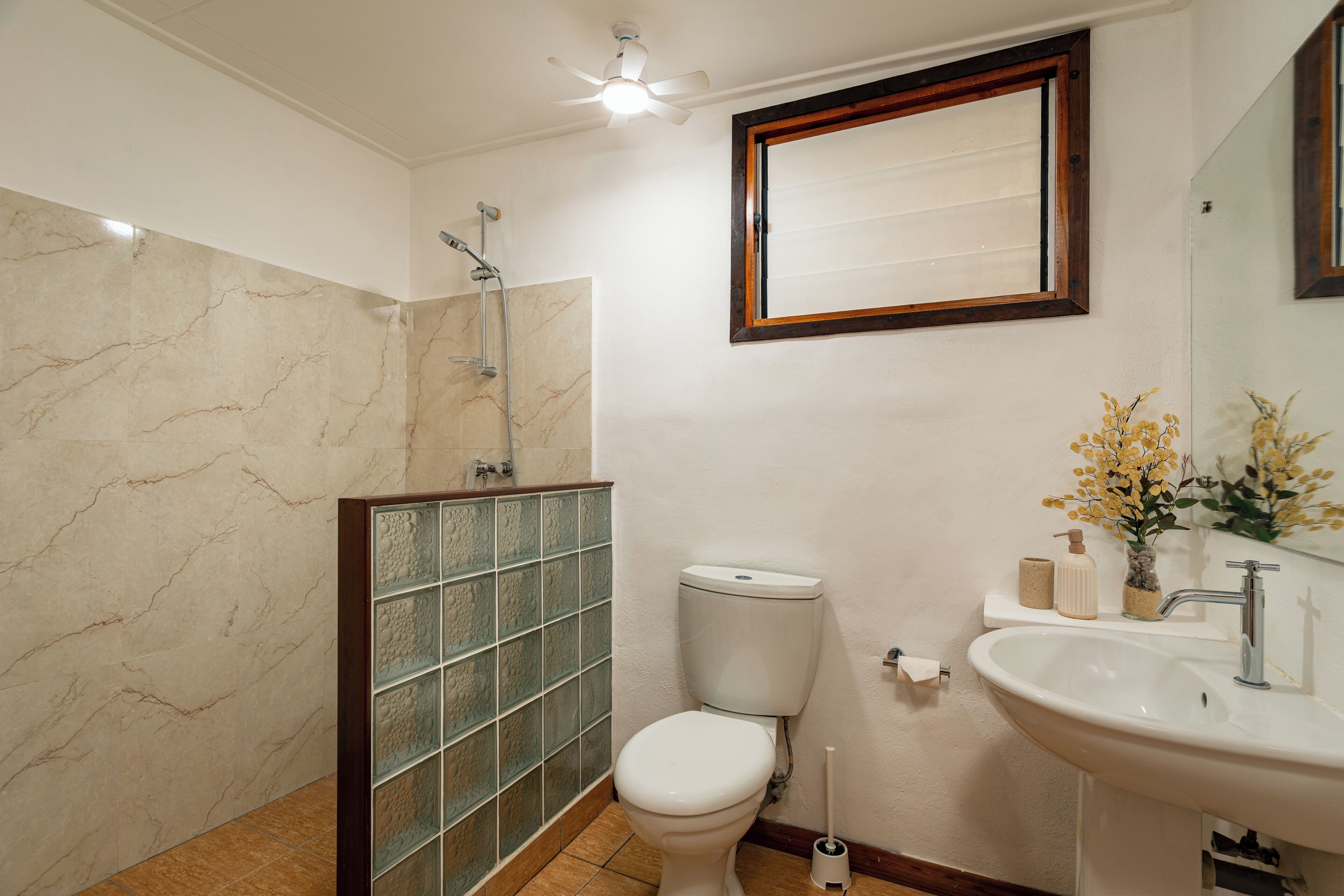 A bathroom with a toilet, sink, shower, and a mirror with a wooden frame.